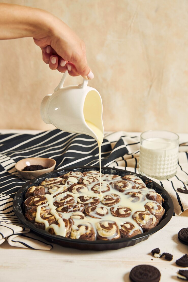 Foto grátis pessoa derramando o creme branco nos deliciosos pãezinhos de canela