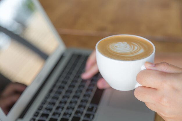 Pessoa digitando em um laptop segurando uma xícara de café