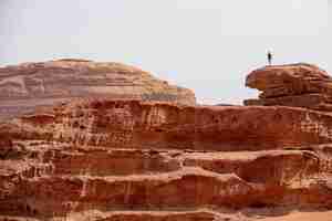 Foto grátis pessoa em pé em um grande penhasco no deserto, sob um céu nublado