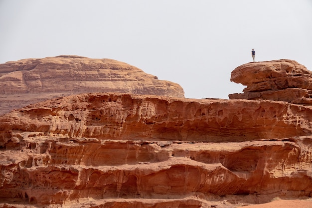 Pessoa em pé em um grande penhasco no deserto, sob um céu nublado