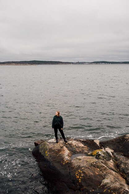 Pessoa em pé sobre uma rocha à beira-mar, olhando para um lado