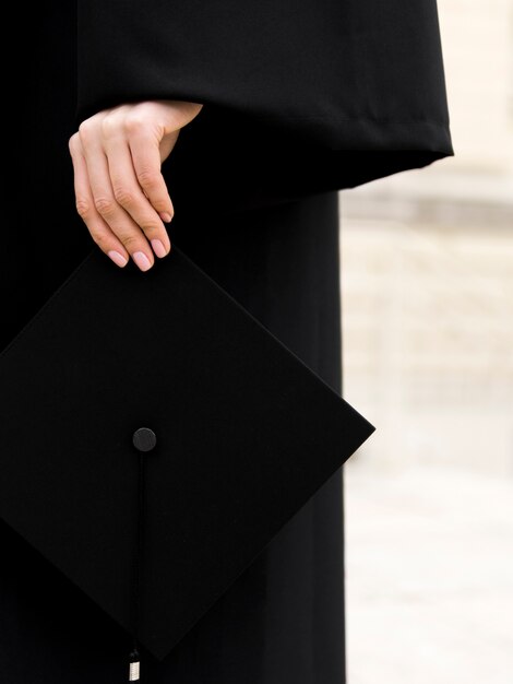 Pessoa em vestido de formatura, segurando seu boné