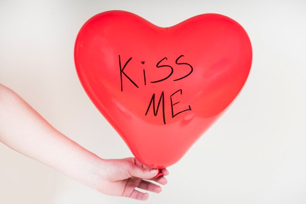 Pessoa segurando balão de coração com Kiss me inscrição