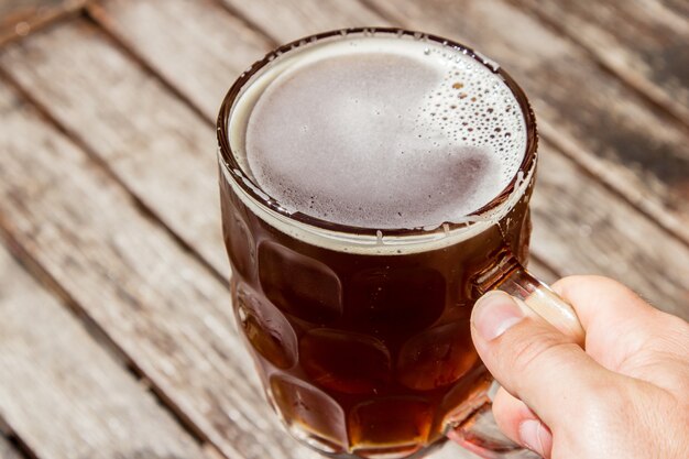 Pessoa segurando um copo de cerveja gelada com uma superfície de madeira