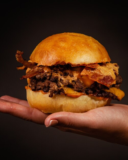 Pessoa segurando um delicioso hambúrguer com carne, queijo amarelo e bacon