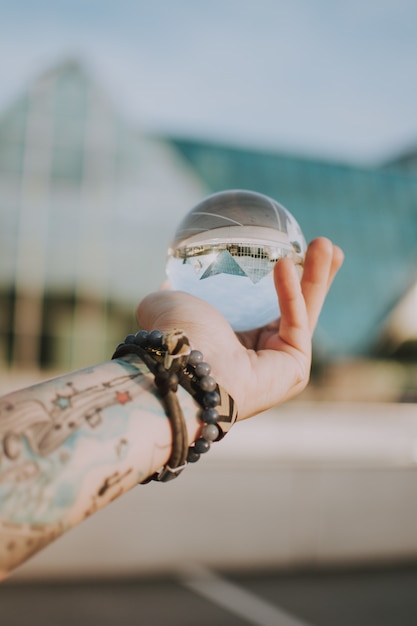 Foto grátis pessoa, segurando uma bola de cristal transparente com o reflexo de um edifício triangular