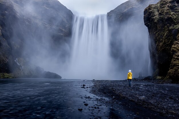 Pessoa vestindo uma jaqueta amarela em pé na cachoeira hipnotizante