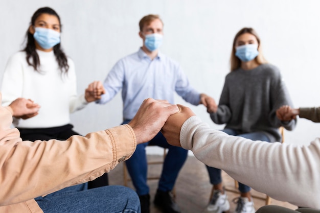 Pessoas com máscaras médicas de mãos dadas em sessão de terapia de grupo