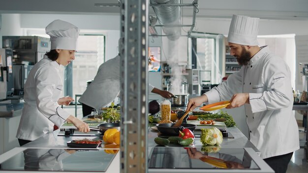 Pessoas cozinhando receita de comida profissional na cozinha do restaurante, usando legumes frescos para preparar refeições gourmet. Equipe diversificada de cozinheiros fazendo autêntico prato de menu para serviço de cozinha gastronômica.