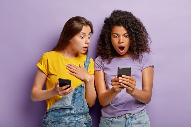 Pessoas da geração milenar olham com expressões chocadas para o telefone celular, rede online, leem mensagem com conteúdo ruim e surpreendente