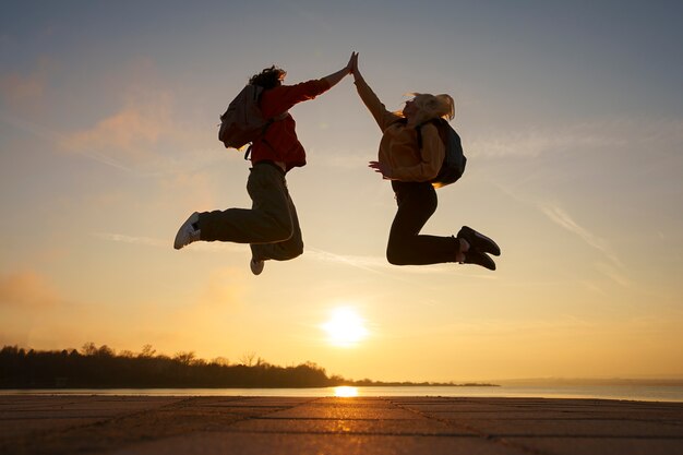 Pessoas de tiro completo pulando ao pôr do sol