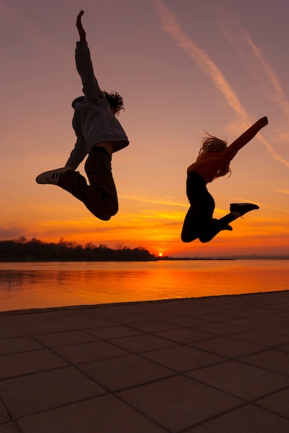 Pessoas de tiro completo pulando ao pôr do sol