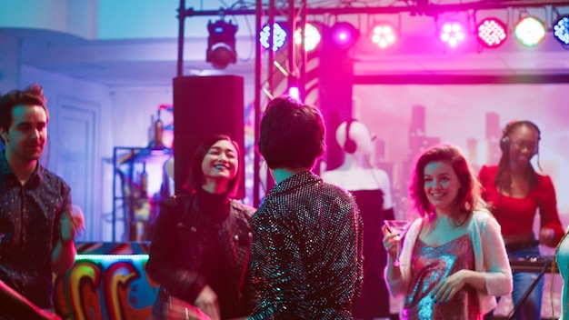 Pessoas descoladas dançando na discoteca com música disco ao vivo, festejando juntas na pista de dança. Jovem grupo de amigos curtindo a vida noturna no clube, indo a discotecas para se divertir. Tiro de tripé.