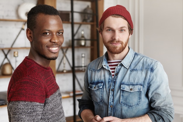 Pessoas e conceito de amizade interracial. dois velhos amigos do sexo masculino que se encontraram no café em pé no interior do café moderno e conversando, ambos olhando com sorrisos felizes