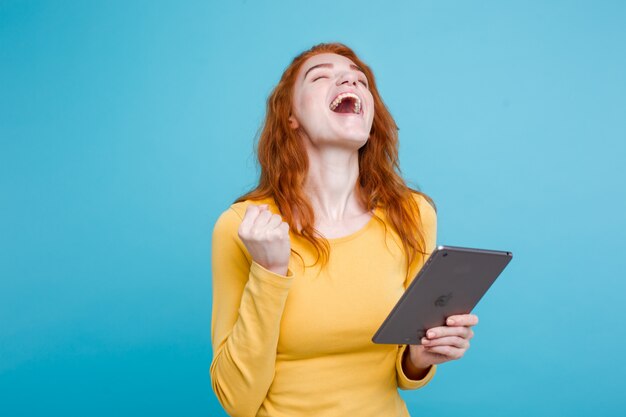 Pessoas e conceito de tecnologia - Close up Retrato jovem atraente atraente redhair menina feliz sorrindo na mesa digital com ganhar algo. Fundo Pastel Azul. Copie o espaço.