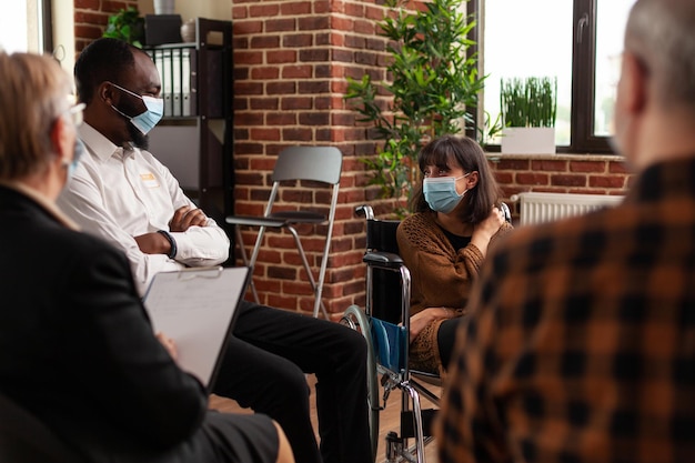 Pessoas e mulher sentada em uma cadeira de rodas, conversando em uma reunião. Pacientes de várias etnias conversando com psiquiatras em terapia de grupo de apoio durante a pandemia covid 19.