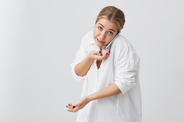 Pessoas e tecnologias. Retrato de mulher branca com cabelo loiro, discutindo o novo projeto com seu parceiro de negócios através do telefone inteligente, olhando com expressão de rosto confuso.