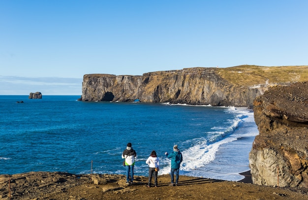 Pessoas em pé na costa cercada pelo mar com o Dyrholaey na Islândia