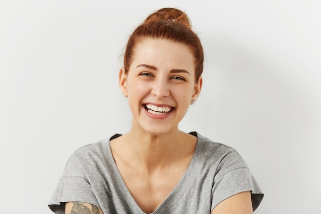 Foto grátis pessoas, juventude e felicidade. retrato da bela mulher caucasiana adolescente feliz vestido casualmente sorrindo amplamente, mostrando os dentes brancos perfeitos, aproveitando o tempo de lazer, passar o fim de semana dentro de casa