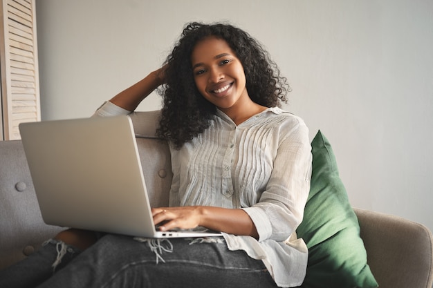 Foto grátis pessoas, lazer, estilo de vida moderno, tecnologia e conceito de aparelhos eletrônicos. mulher jovem e atraente de raça mista, feliz, desfrutando de comunicação online, tendo um vídeo chat usando o laptop em casa