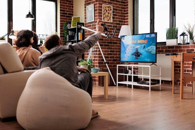 Foto grátis pessoas multiculturais sentadas no sofá na sala de estar enquanto jogam jogos de simulação espacial no dispositivo de console. diversos amigos sentados em casa enquanto desfrutam de videogames juntos.