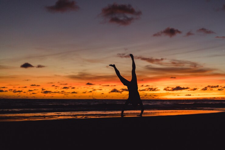 Foto grátis pessoas na costa do oceano ao pôr do sol. homem salta contra o pano de fundo do sol poente