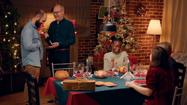 Pessoas positivas pacíficas se reuniram em torno da mesa de jantar de natal na sala de estar. membros da família sorridentes felizes comemorando as férias de inverno tradicionais com comida caseira e bebidas alcoólicas.