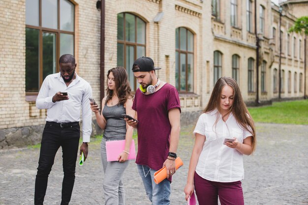 Pessoas que olham para smartphones de pé lá fora