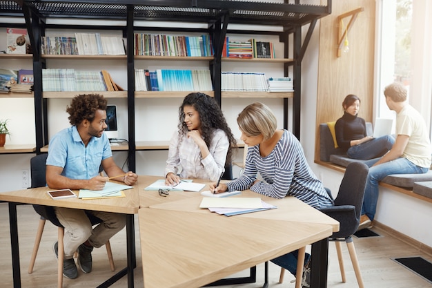 Pessoas que trabalham em equipe. Três parceiros de negócios jovem perspectiva sentado na biblioteca, discutindo sobre detalhes e lucros do projeto de inicialização. Conceito de trabalho em equipe.