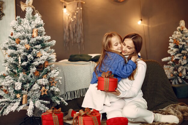 Pessoas reparando pelo Natal. Mãe brincando com sua filha. Família está descansando em uma sala festiva. Criança com um suéter azul.