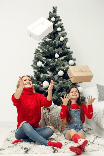 Pessoas reparando pelo Natal. Mãe brincando com sua filha. Família está descansando em uma sala festiva. Criança com um suéter vermelho.