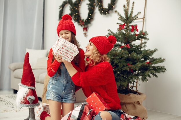 Pessoas reparando pelo Natal. Mãe brincando com sua filha. Família está descansando em uma sala festiva. Criança com um suéter vermelho.