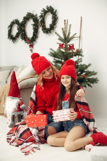 Pessoas reparando pelo Natal. Mãe brincando com sua filha. Família está descansando em uma sala festiva. Criança com um suéter vermelho.