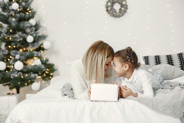 Pessoas reparando pelo Natal. Mãe brincando com sua filha. Família está descansando em uma sala festiva. Criança com um suéter.