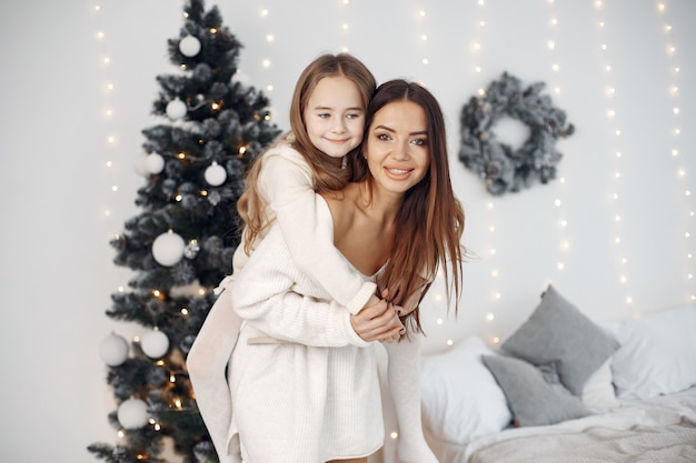 Pessoas reparando pelo Natal. Mãe brincando com sua filha. Família está descansando em uma sala festiva. Menina de vestido branco.