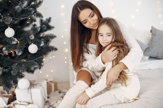 Pessoas reparando pelo Natal. Mãe brincando com sua filha. Família sentada na cama. Menina de vestido branco.