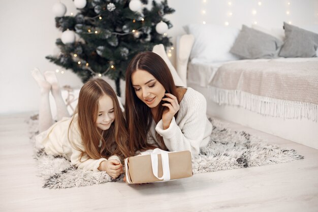 Pessoas reparando pelo Natal. Mãe brincando com sua filha. Família sentada perto da árvore de Natal. Menina de vestido branco.