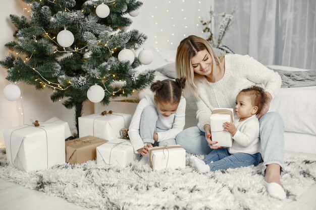 Pessoas reparando pelo Natal. Mãe brincando com suas filhas. Família está descansando em uma sala festiva. Criança com um suéter.