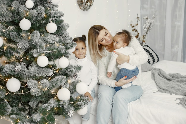 Pessoas reparando pelo Natal. Mãe brincando com suas filhas. Família está descansando em uma sala festiva. Criança com um suéter.