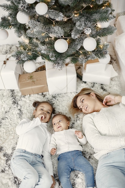 Pessoas reparando pelo Natal. Mãe brincando com suas filhas. Família está descansando em uma sala festiva. Criança com um suéter.