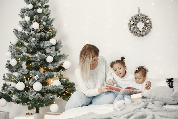 Pessoas reparando pelo Natal. Mãe brincando com suas filhas. Família está descansando em uma sala festiva. Criança com um suéter.