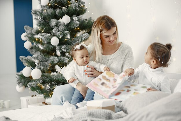 Pessoas reparando pelo Natal. Mãe brincando com suas filhas. Família está descansando em uma sala festiva. Criança com um suéter.