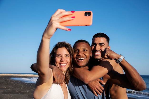 Pessoas sorridentes de tiro médio tomando selfie na praia