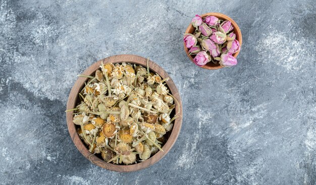 Pétalas de rosa secas e camomilas em tigelas de madeira.