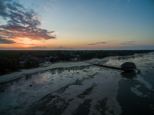 Píer na praia à beira-mar sob o pôr do sol em Zanzibar, África