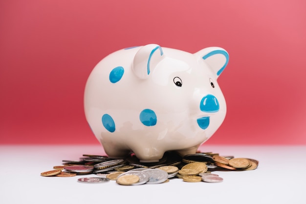 Piggybank cerâmico manchado sobre moedas na frente do fundo vermelho