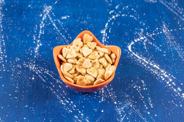 Pilha de biscoitos salgados em forma de coração colocados em uma tigela de laranja.