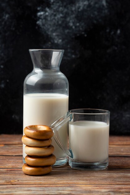 Pilha de biscoitos, uma garrafa de leite e um copo de leite na mesa de madeira.