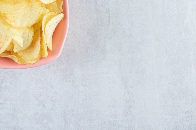 Pilha de chips crocantes salgados colocados em uma tigela rosa na pedra.