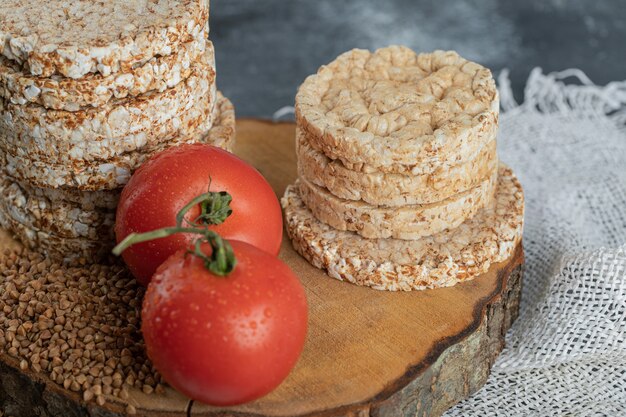 Pilha de pão crocante, tomate e trigo sarraceno cru na peça de madeira